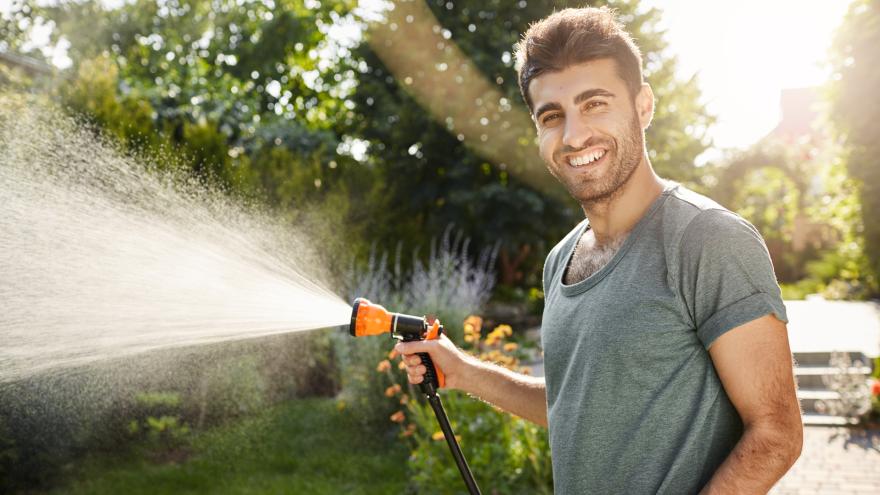 Mann mit Gartenschlauch lacht und gießt Garten