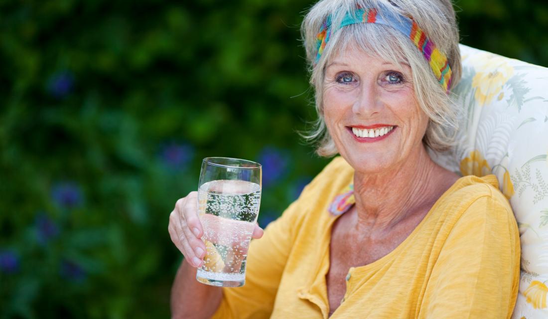 Dame lächelt mit Wasserglas in der Hand